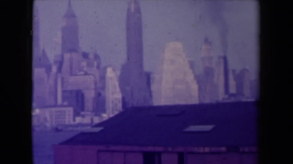 France-attributed 1945 8mm frame with a soft distant urban skyline, prominent vertical tower form, and dark foreground rooftop.