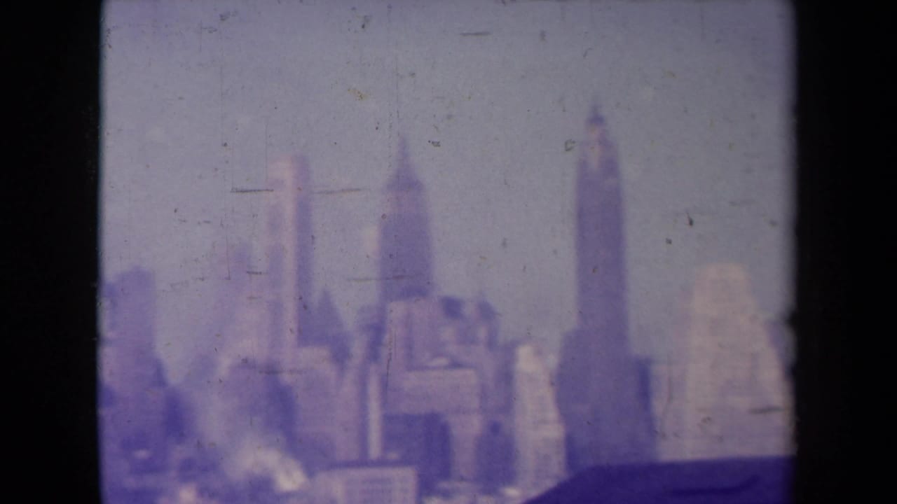 Soft, purple-tinted city skyline with tall buildings seen beyond a dark rooftop edge.