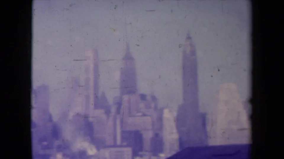 Hazy 8mm view of a distant urban skyline in France, with tall building forms and purple color shift over a dark foreground roof.