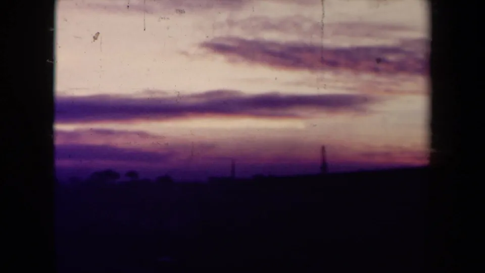 Vintage 8mm sunset view in France, showing broad purple cloud bands above a dark horizon and heavy film texture.