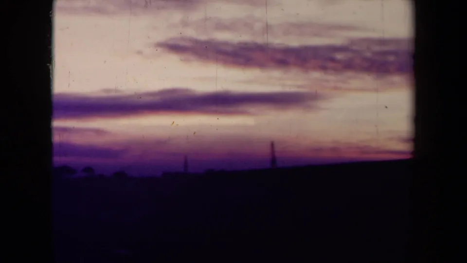 Final sunset frame with layered purple clouds, a dark skyline, and visible 8mm gate edges and scratches.