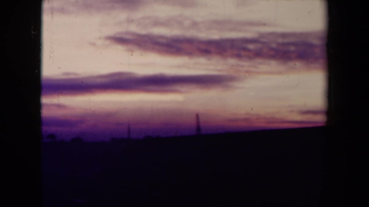 Purple and pink sunset sky above a dark empty field with faint horizon structures.