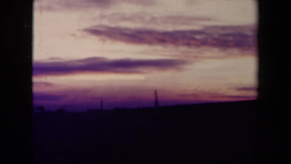 1945 France 8mm frame showing a purple-pink sunset over a dark open field, with faint vertical shapes on the horizon.