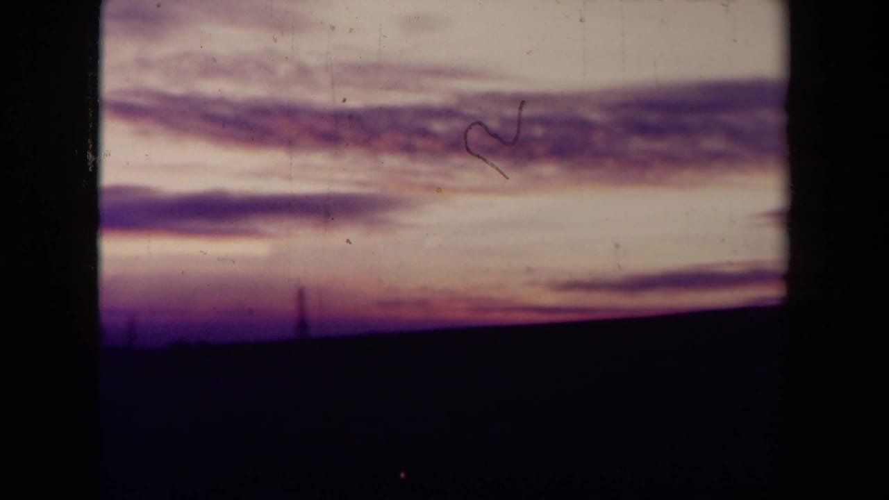1945 France 8mm frame with streaked dusk clouds, a dark empty foreground, faint horizon structures, and visible film wear.