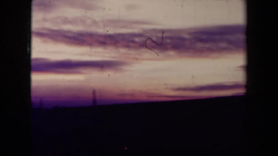 1945 France 8mm frame with streaked dusk clouds, a dark empty foreground, faint horizon structures, and visible film wear.