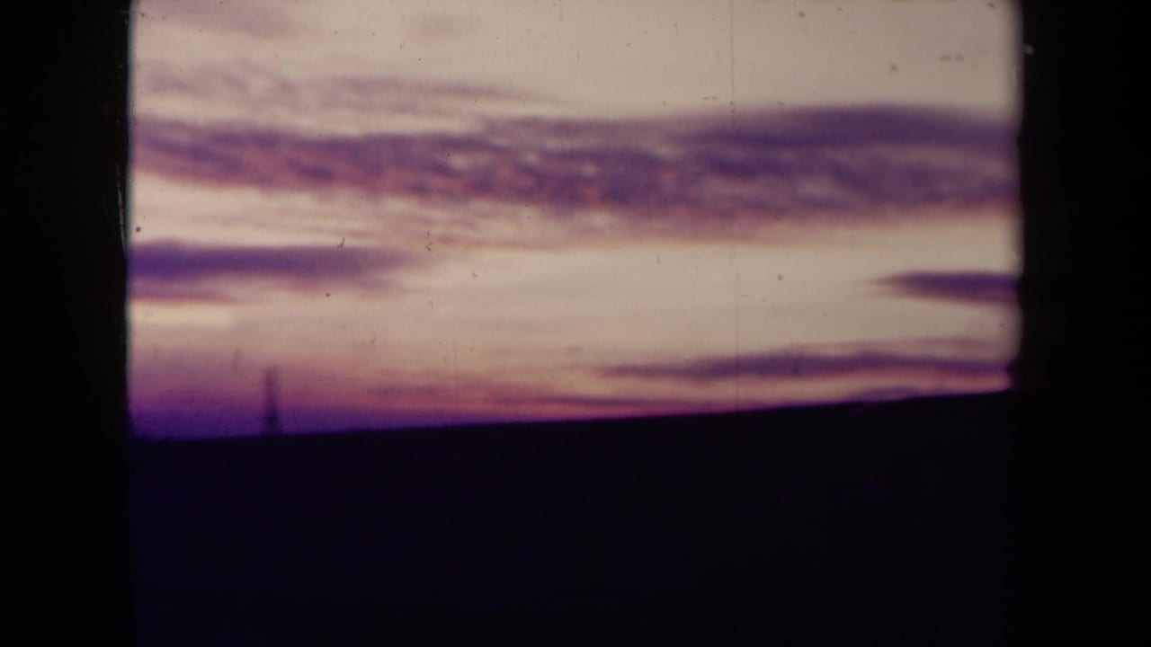 1945 France 8mm frame showing a faded pink sunset, purple cloud layers, and a nearly black empty field below.