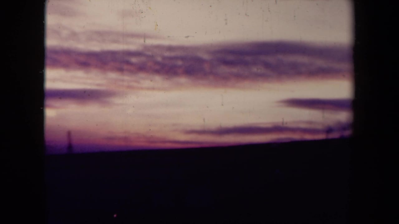 Distant sea horizon and layered sunset clouds seen through dark film gate edges.
