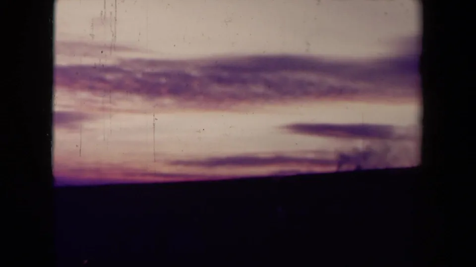 1940s France 8mm view of a calm sea horizon under fading sunset clouds, framed by dark film borders and soft color shift.