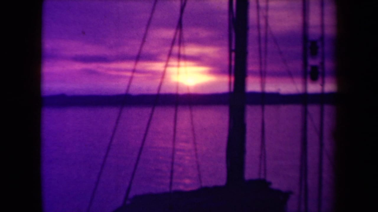 1940s France 8mm boatboard view of the sun near the horizon, with mast and rigging silhouetted against purple clouds over the sea.