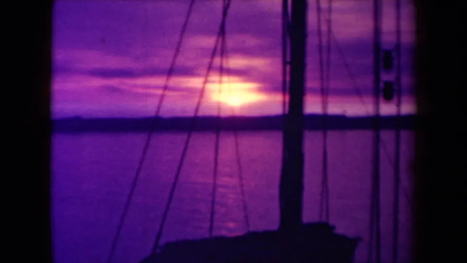 1940s France 8mm boatboard view of the sun near the horizon, with mast and rigging silhouetted against purple clouds over the sea.