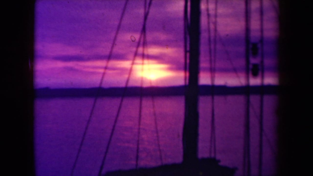 1940s France 8mm frame showing a warm sun near the sea horizon, seen past boat rigging and dark vertical mast shapes.