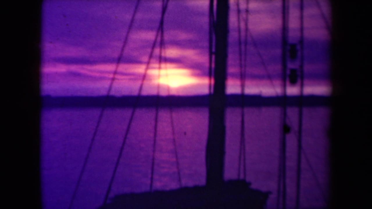 Ocean sunset framed by mast, rigging, and a dark boat silhouette.