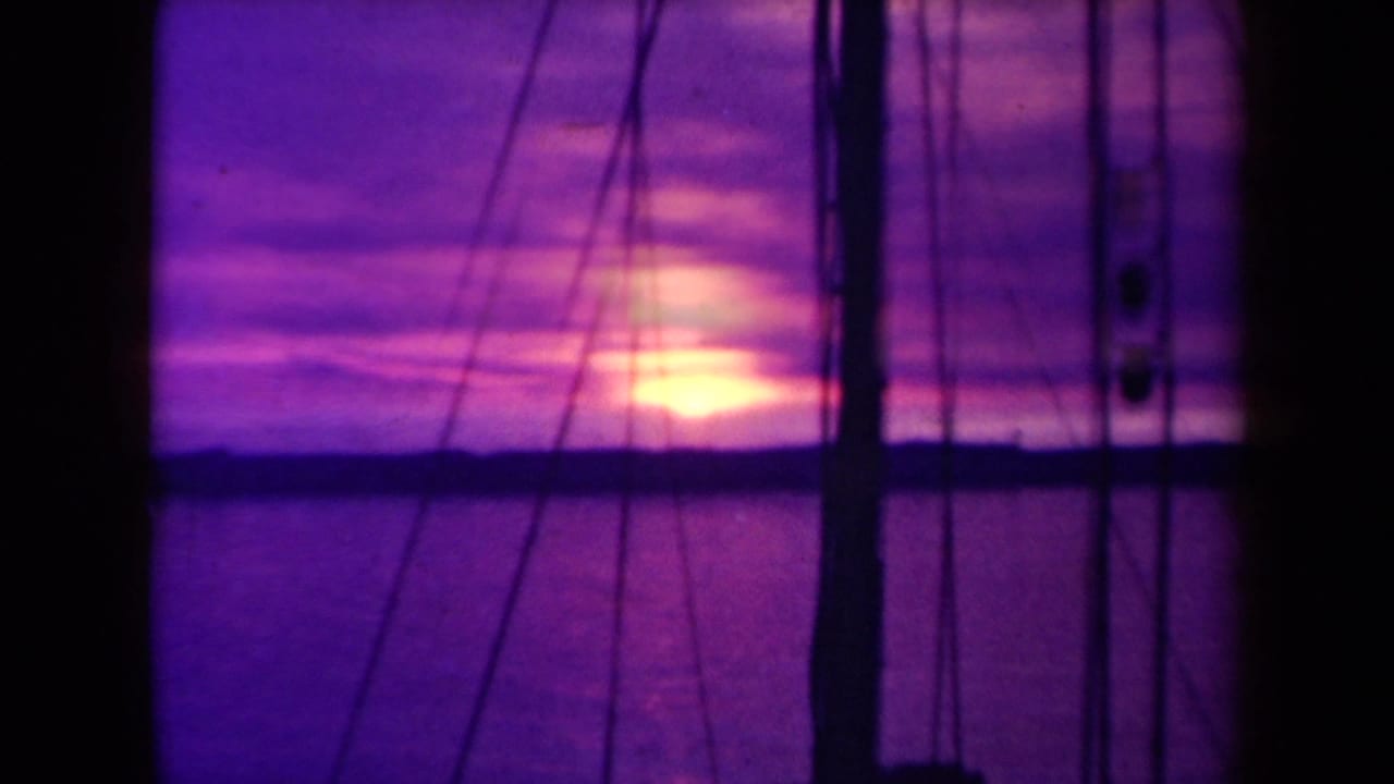 1945 France 8mm sunset view with bright reflected light on the ocean and dark sailboat rigging in front.