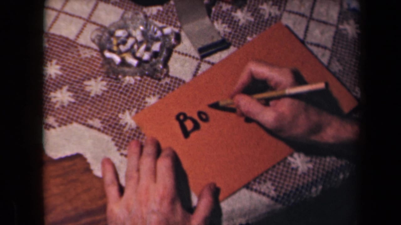 A hand writes the letters Bo on a brown envelope while another hand holds it steady.