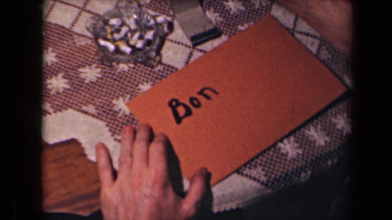 The name Bon appears in black ink on a brown envelope in a French 1945 home-movie close-up of hands at a table.