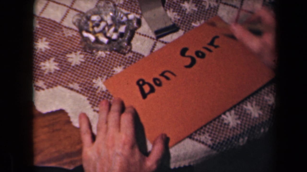 The completed “Bon Soir” greeting is visible on the brown card, with hands, tablecloth, and ashtray nearby in the 1945 France clip.
