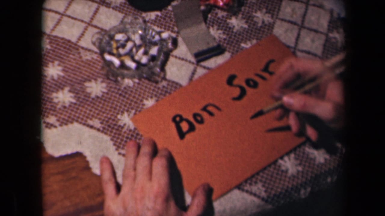 The dip pen adds a dark finishing mark beneath “Bon Soir” on the brown card while the tabletop ashtray remains visible.