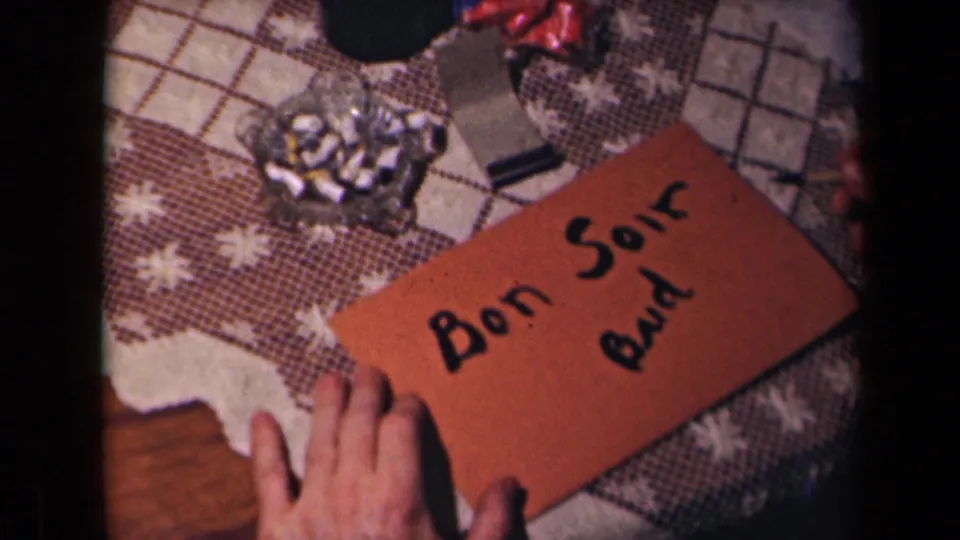 The final frame shows the orange envelope with Bon Soir and additional black writing on a patterned table beside a glass ashtray.