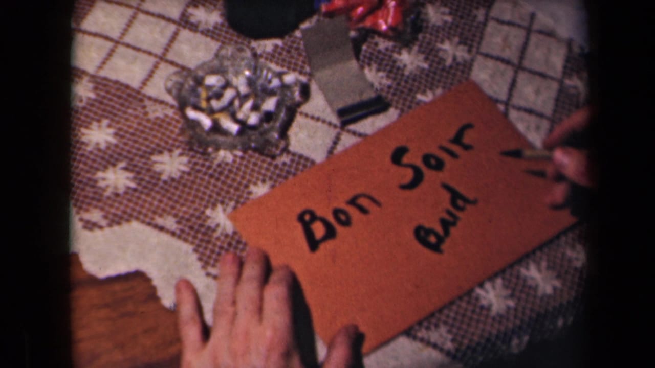 Hands hold a brown card while black lettering reads "Bon Soir" and "Bud" on a patterned tablecloth.