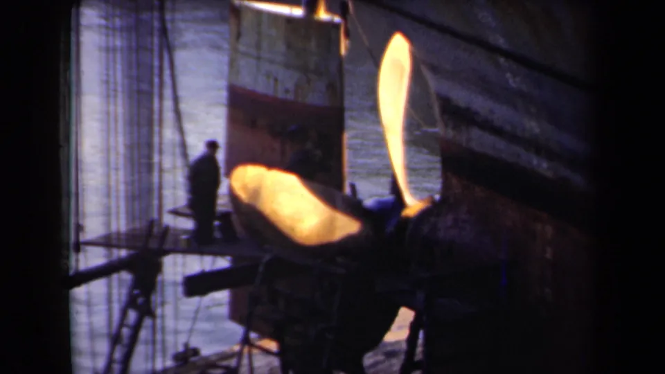 The final frame repeats the close view of the exposed propeller and hull, with a distant worker standing beside dock rigging.