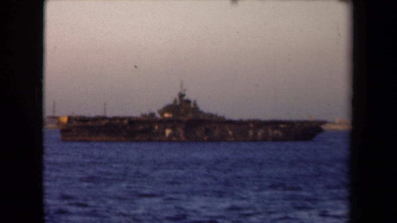 Large naval vessel viewed across water under a pale sky.