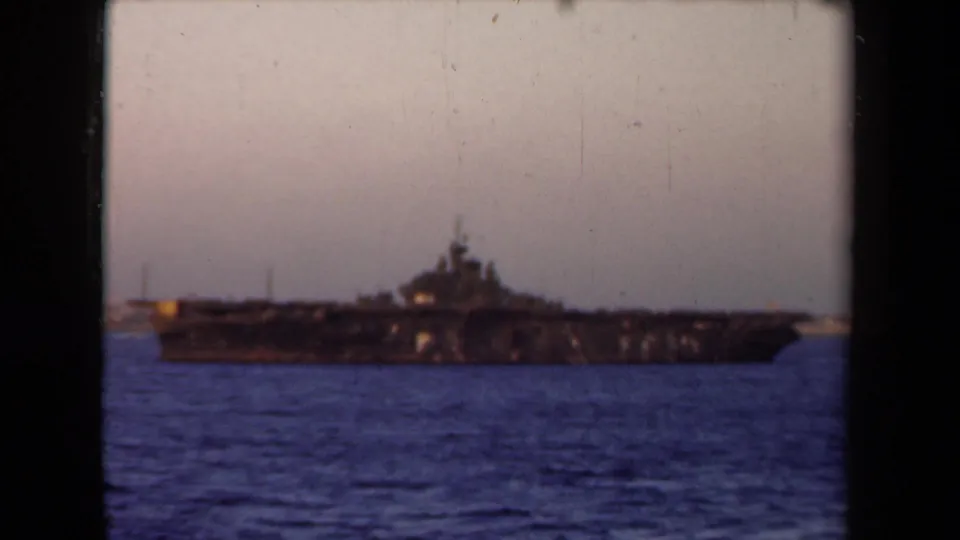 A large naval vessel remains in view near the horizon in 1946 Netherlands harbor footage, with blue water and visible 8mm frame edges.