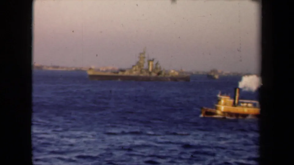 A small yellow tugboat with a smoking stack crosses the foreground while a larger vessel sits beyond it in the 1946 Netherlands harbor scene.