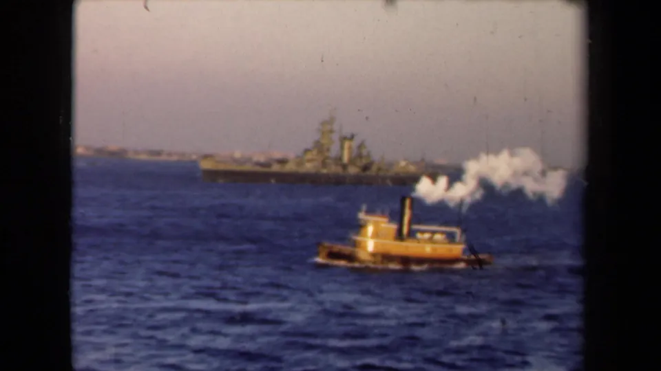 A yellow tugboat throws white smoke or spray across the water, with a distant warship visible in the Netherlands 1946 home-movie frame.