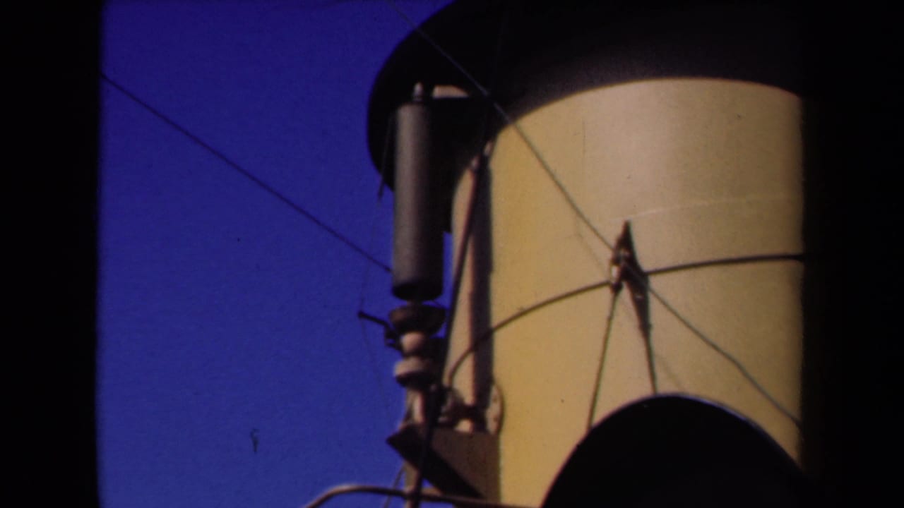 Close 8mm view of a yellow-and-black ship funnel and attached cylindrical fitting against blue sky in the Netherlands clip.