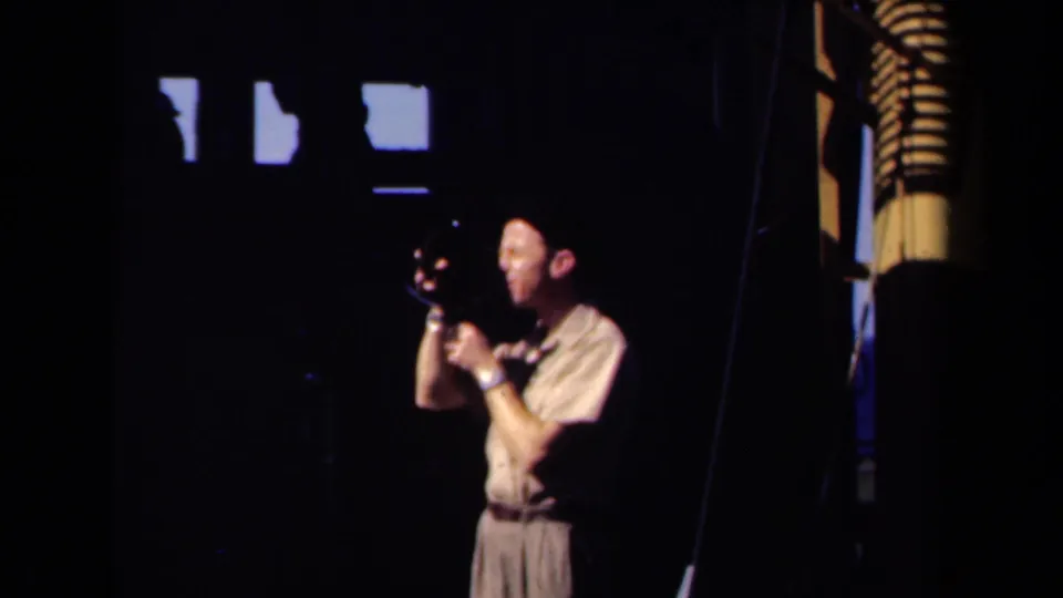 In 1946 Netherlands home-movie footage, a man in a pale shirt and dark hat appears to film with a small camera inside a shadowed interior with bright high windows.