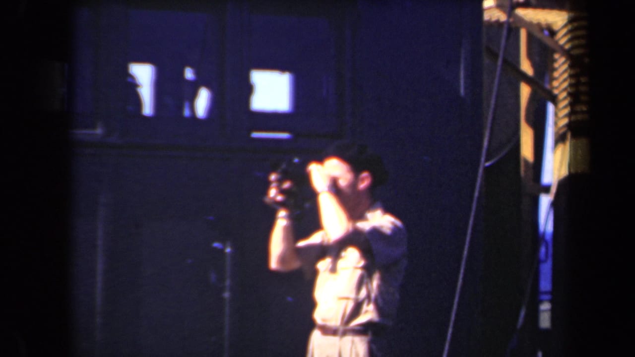 Man raises one hand to his forehead while holding a camera in a dark room.