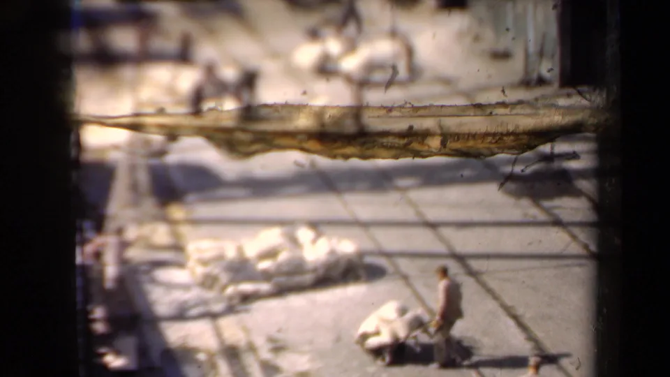 Distant workers in a flour-yard scene move large sacks and a wheelbarrow across sunlit concrete in 1946 archival footage.