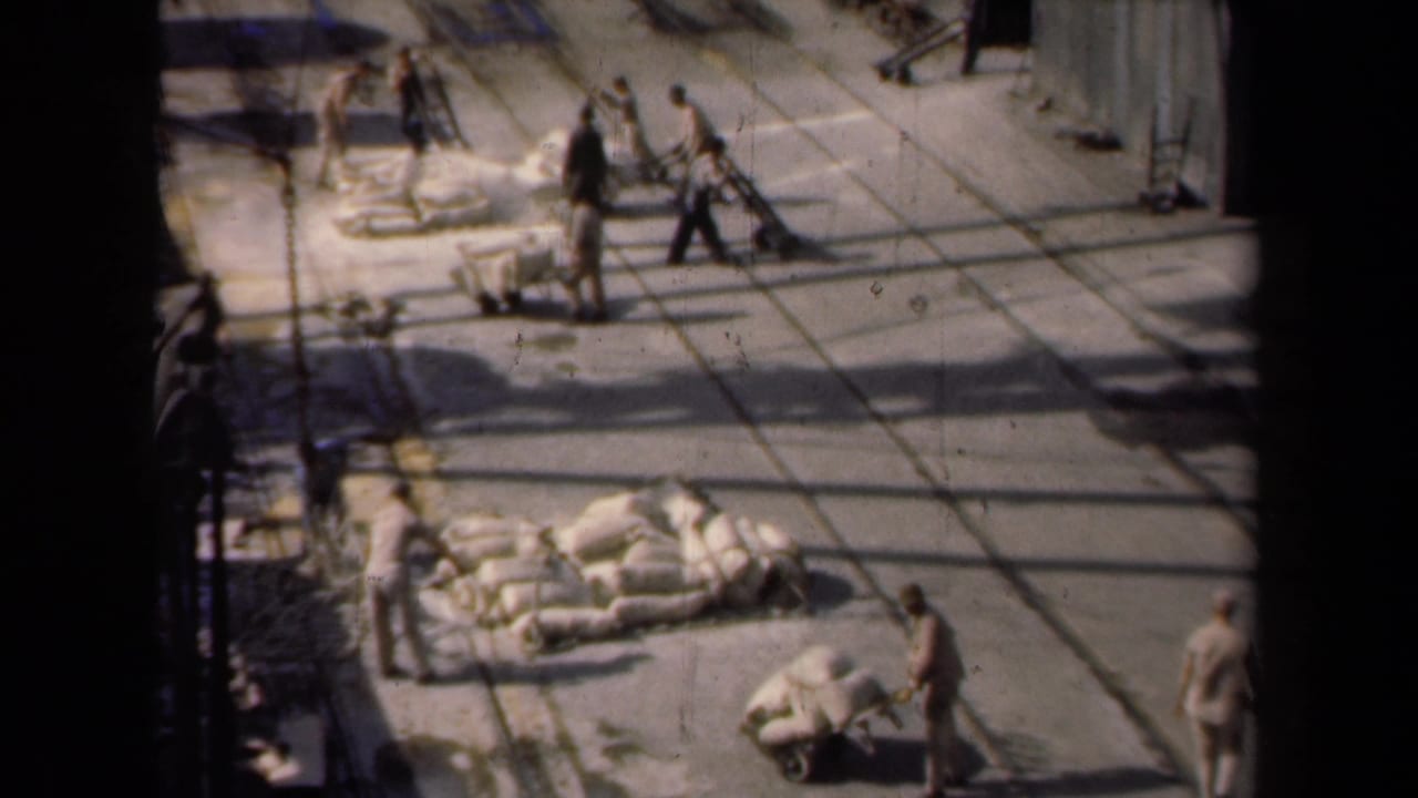 High-angle 1946 Netherlands 8mm frame showing workers, hand carts, and piles of white sacks in a paved yard.