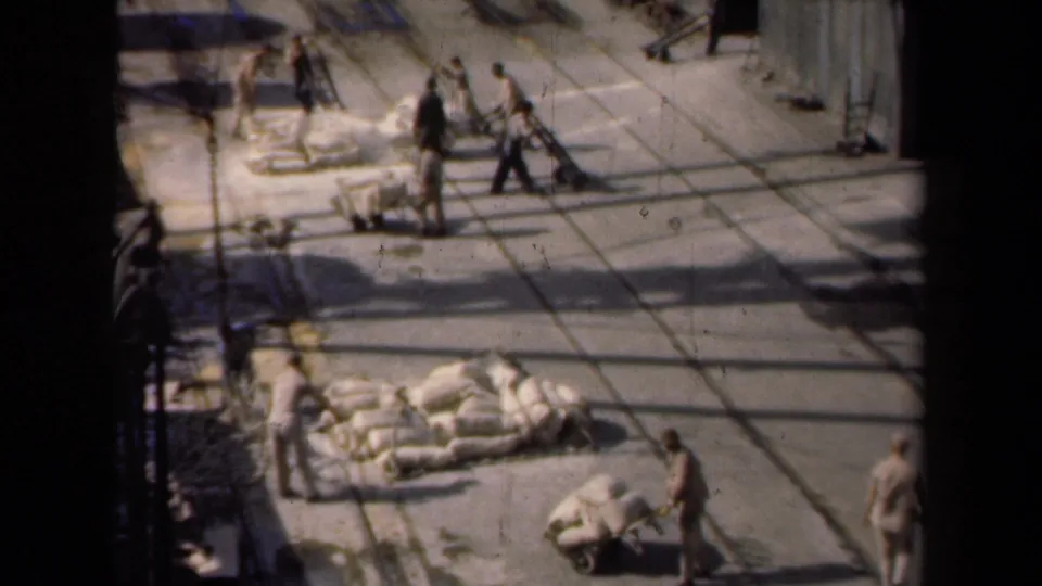 High-angle 1946 Netherlands 8mm frame showing workers, hand carts, and piles of white sacks in a paved yard.