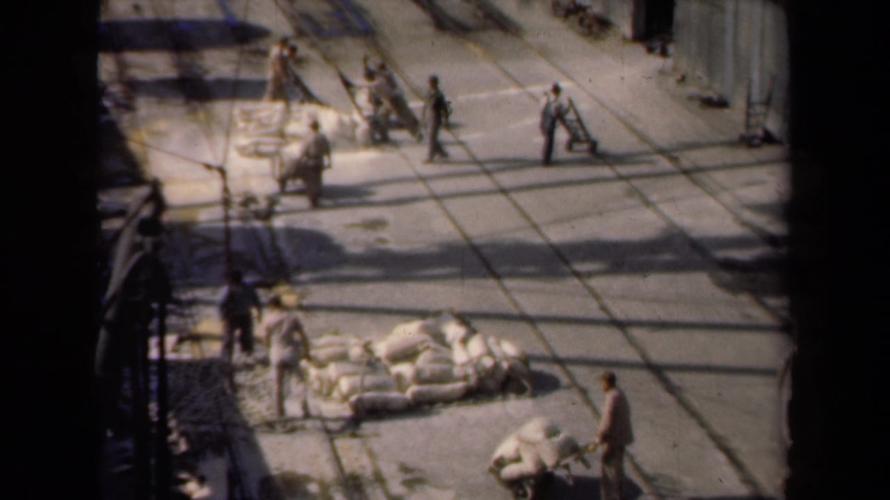 High-angle Netherlands work-yard scene from 1946 with men near sacks, carts, and long shadows on pavement.