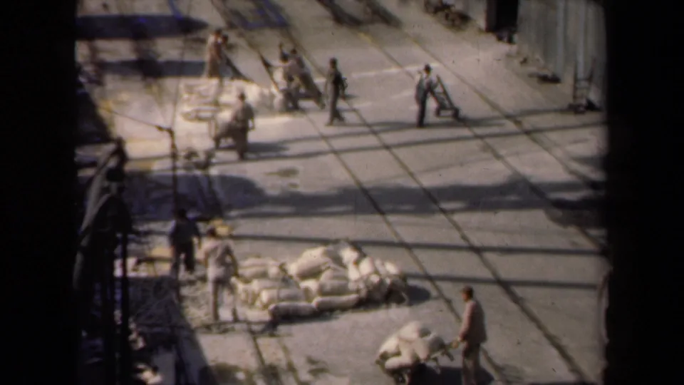 High-angle Netherlands work-yard scene from 1946 with men near sacks, carts, and long shadows on pavement.