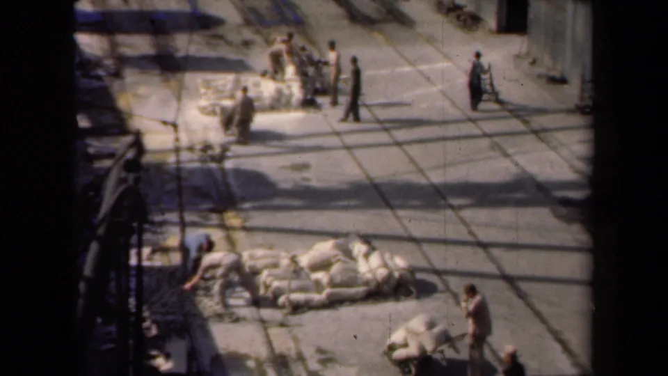 1946 Netherlands 8mm frame with workers moving through a paved industrial yard and handling large white sacks.