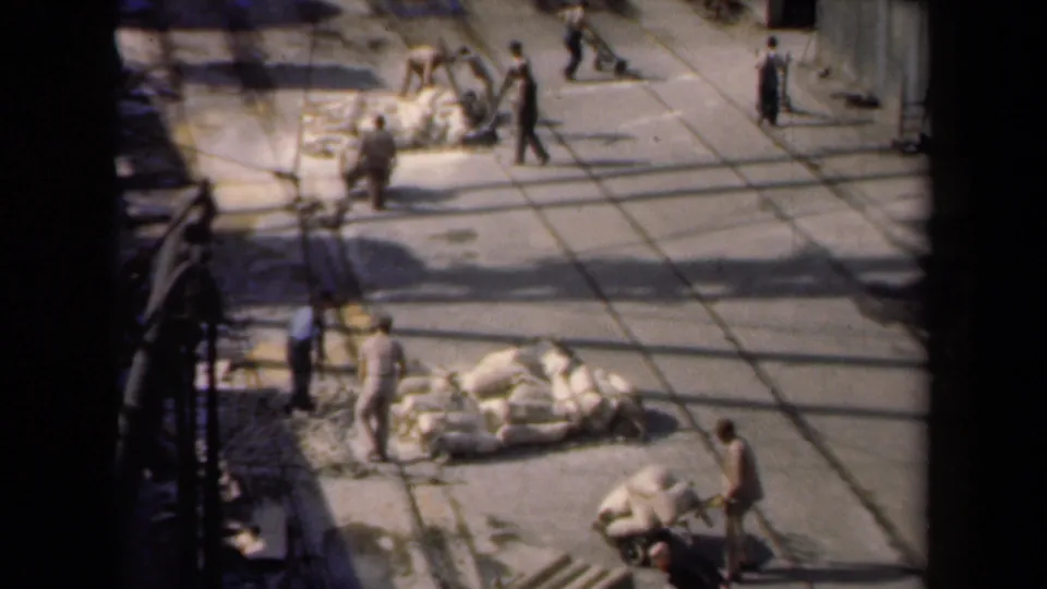 High-angle 1946 Netherlands work scene showing workers, carts, sacks, and strong shadows across the yard.