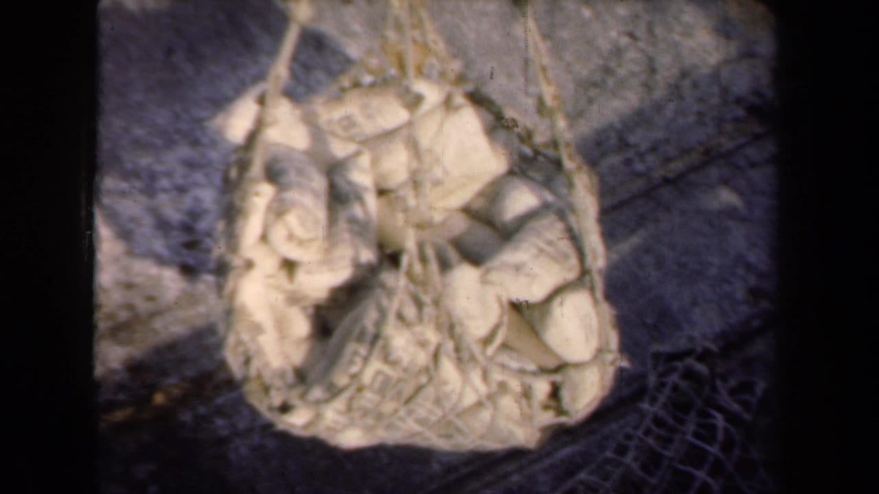 1946 Netherlands 8mm frame showing burlap sacks packed into braided netting, viewed from above over a paved industrial surface.