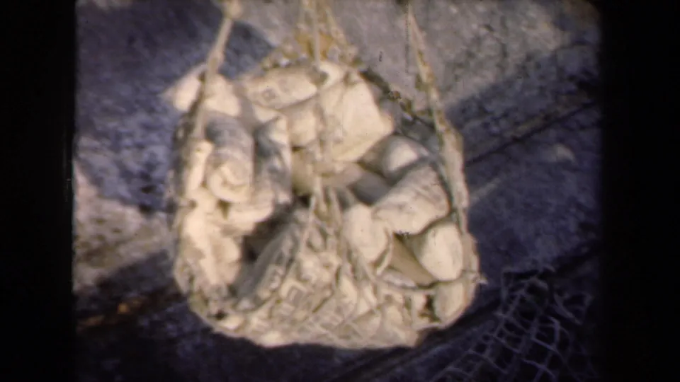 1946 Netherlands 8mm frame showing burlap sacks packed into braided netting, viewed from above over a paved industrial surface.