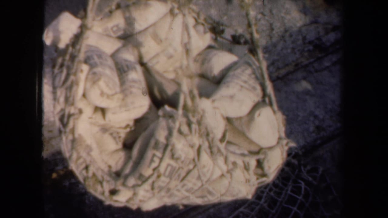 1946 Netherlands footage frame with tan burlap sacks and rope netting filling most of the view above the industrial lot.