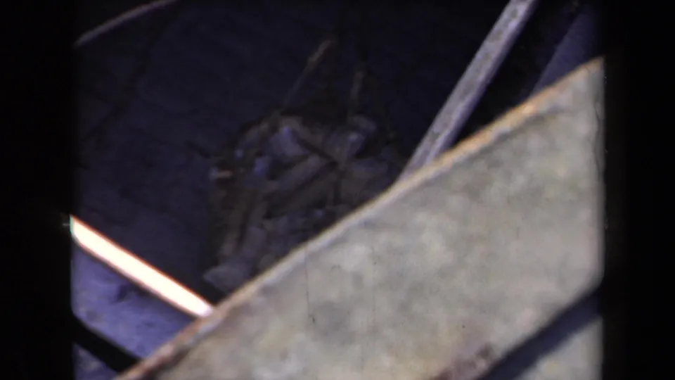 Soft 8mm frame showing cargo gear or sacks partly obscured by a diagonal rail and pale ship structure.