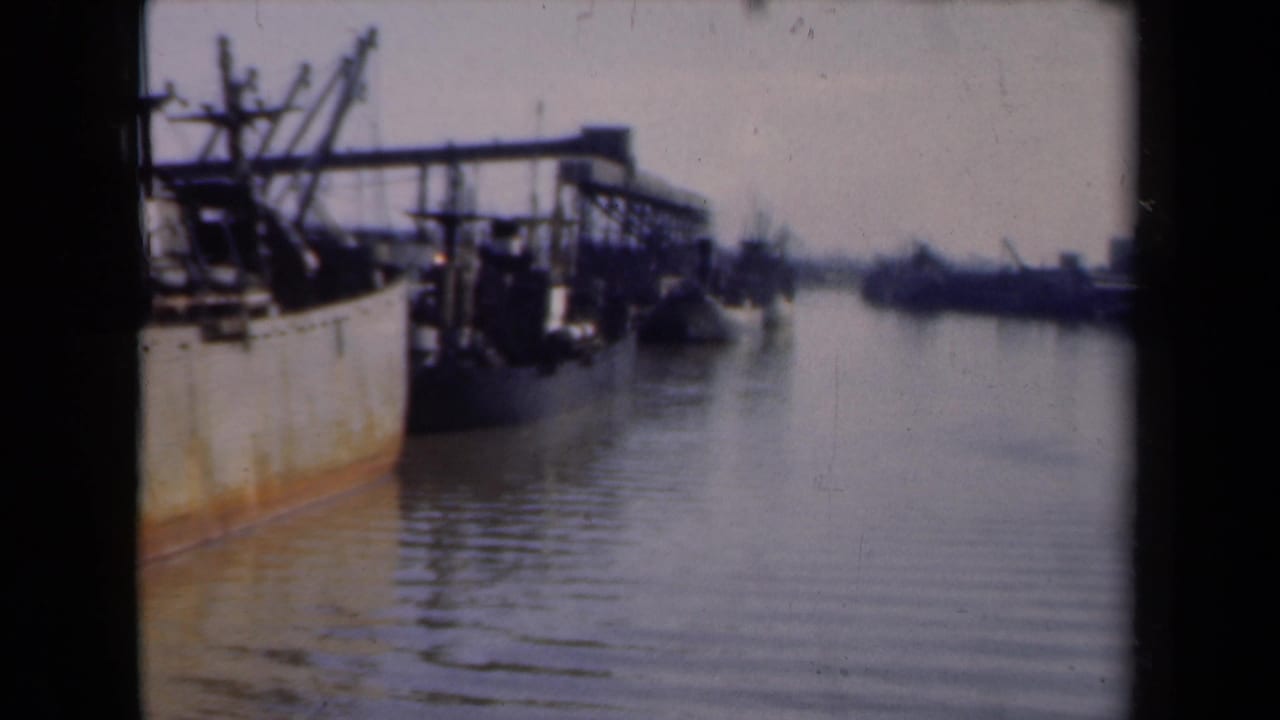 Harbor waterway with a large moored ship at left and dock structures beyond.