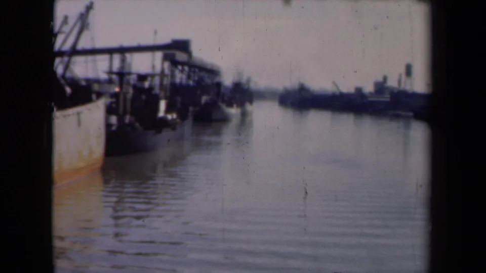 Dutch harbor scene from 1946 showing dockside structures, moored vessels, calm water, and distant industrial ship silhouettes.