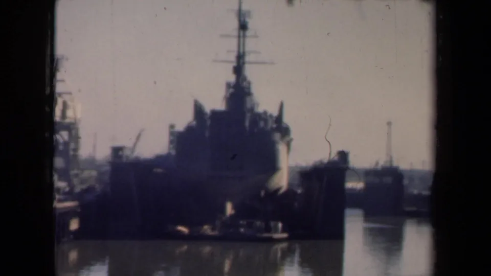 1946 Netherlands harbor frame with a large naval or cargo vessel, tall mast, dock edge, and water visible beside the ship.