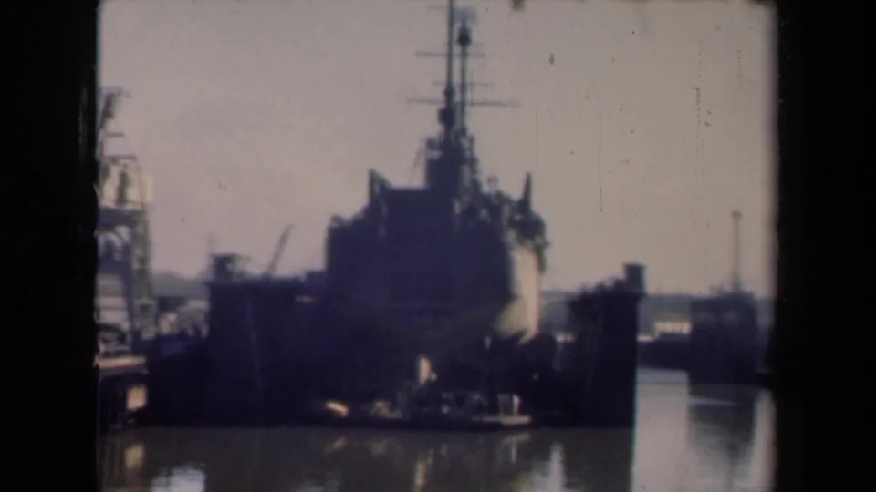 1946 Netherlands 8mm frame of a large ship entering port, viewed head-on with dock machinery and calm water around it.