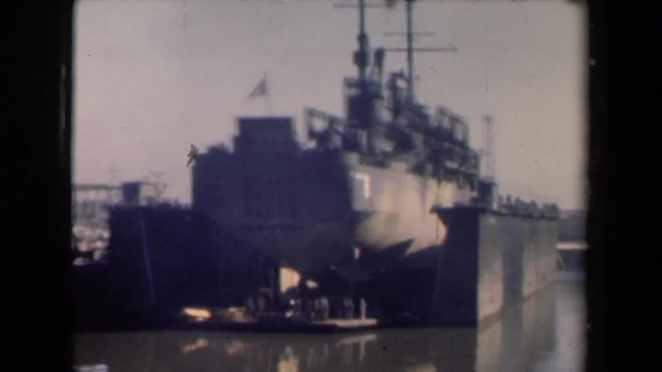 1946 Netherlands 8mm frame of a large vessel in harbor, seen from an angle with a small flag, superstructure, and dockside setting.