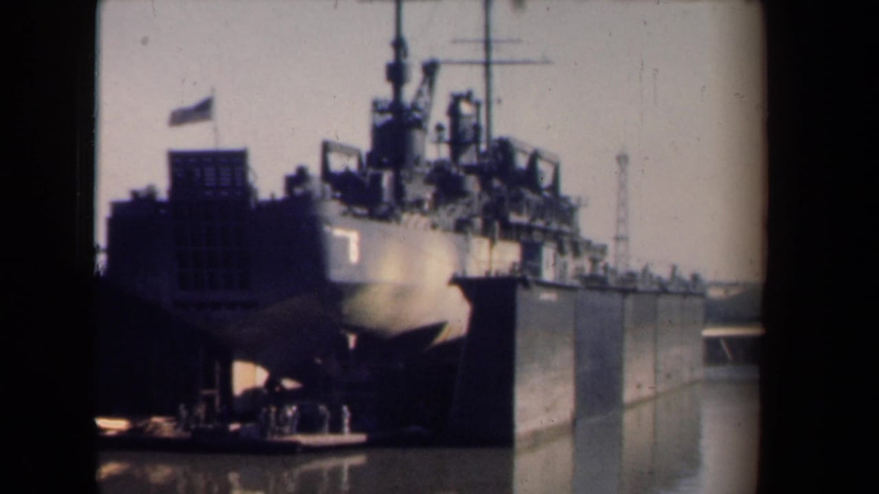 1946 Netherlands home-movie frame showing a large military vessel at a harbor, with bow, mast, and upper deck structures visible.