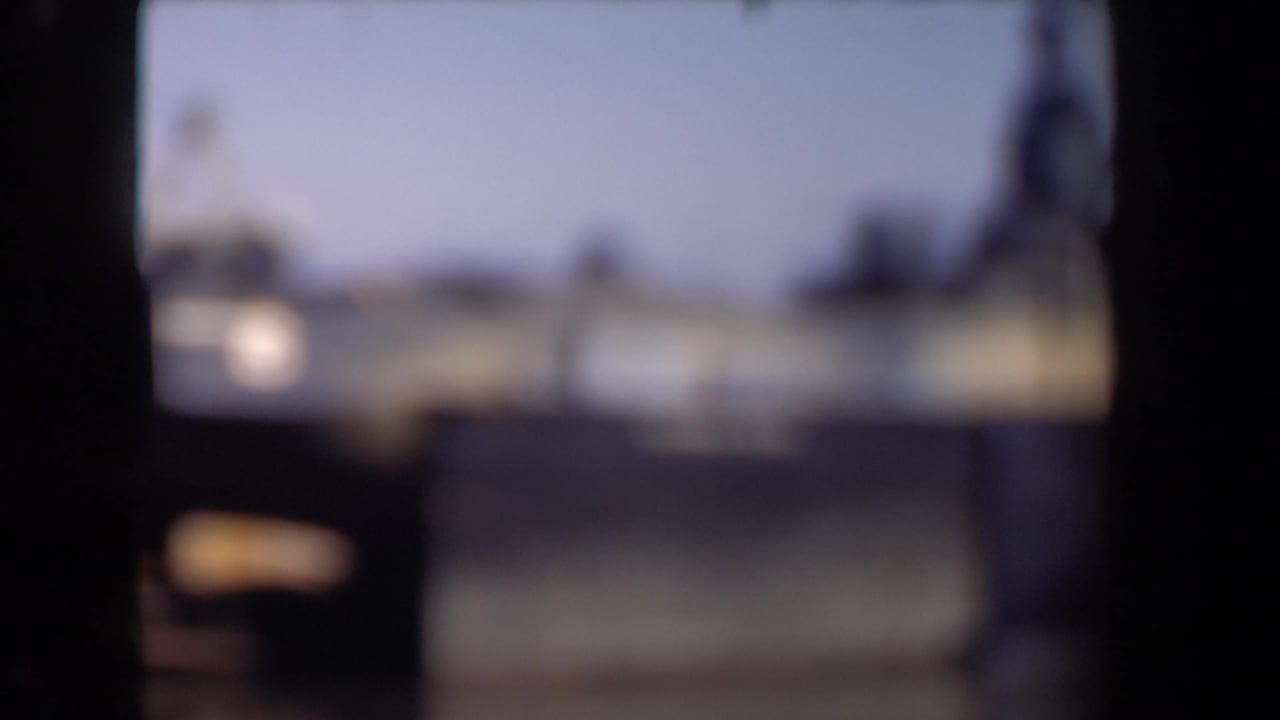 Soft, out-of-focus 8mm frame from the Netherlands clip, showing a blurred harbor and possible vessel forms behind dark scan borders.