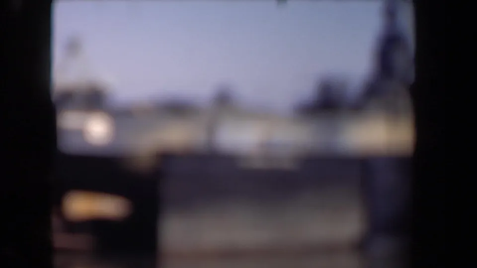 Soft, out-of-focus 8mm frame from the Netherlands clip, showing a blurred harbor and possible vessel forms behind dark scan borders.